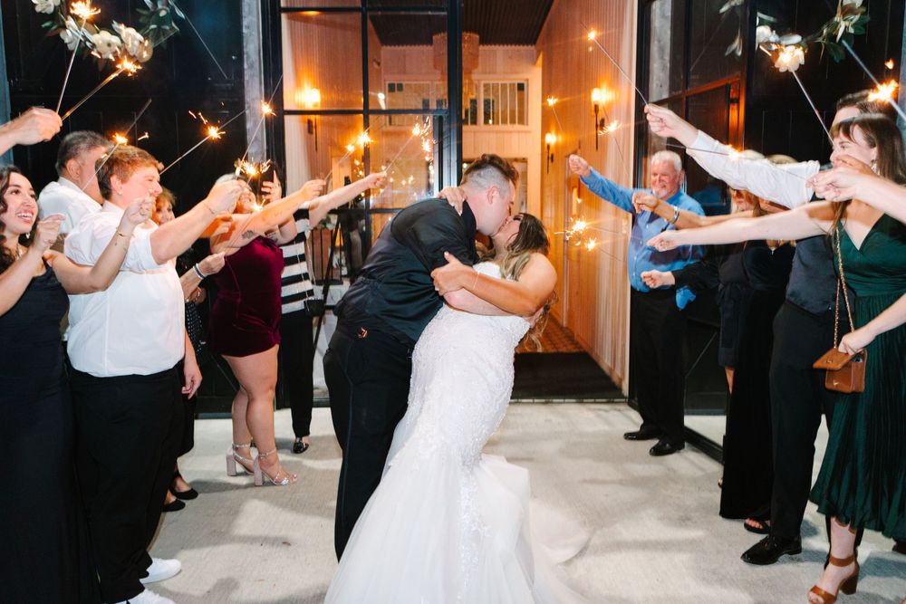 Couple embraces during sparkler exit as wedding guests create a magical departure tunnel.