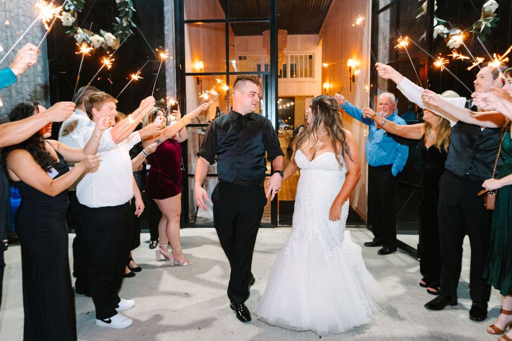 Wedding couple exits through sparkler tunnel held by guests in formal attire.