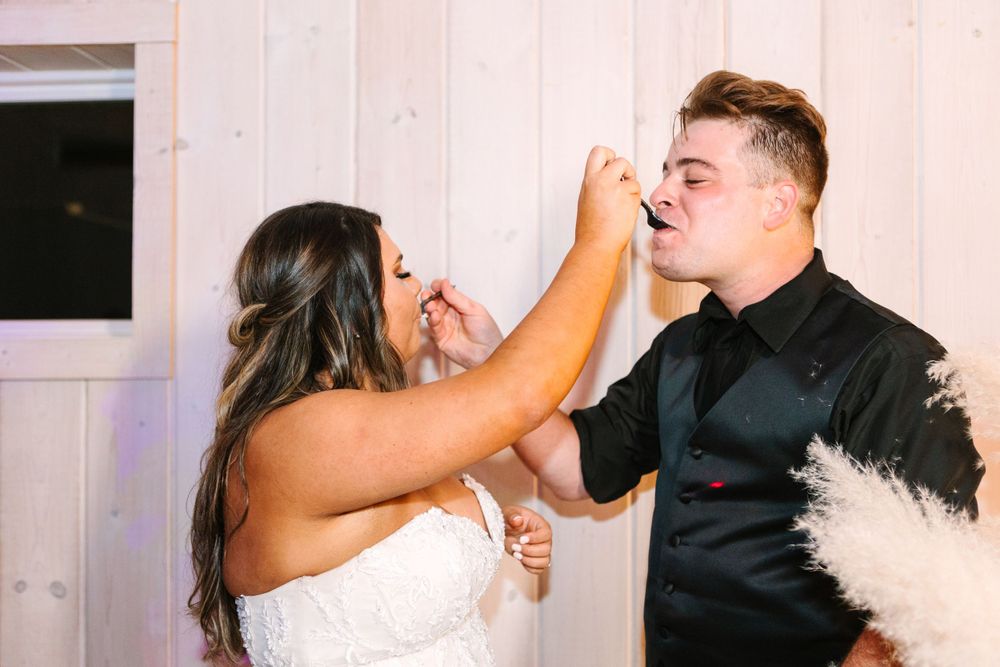 Wedding couple playfully feeds each other cake during traditional cake cutting ceremony.