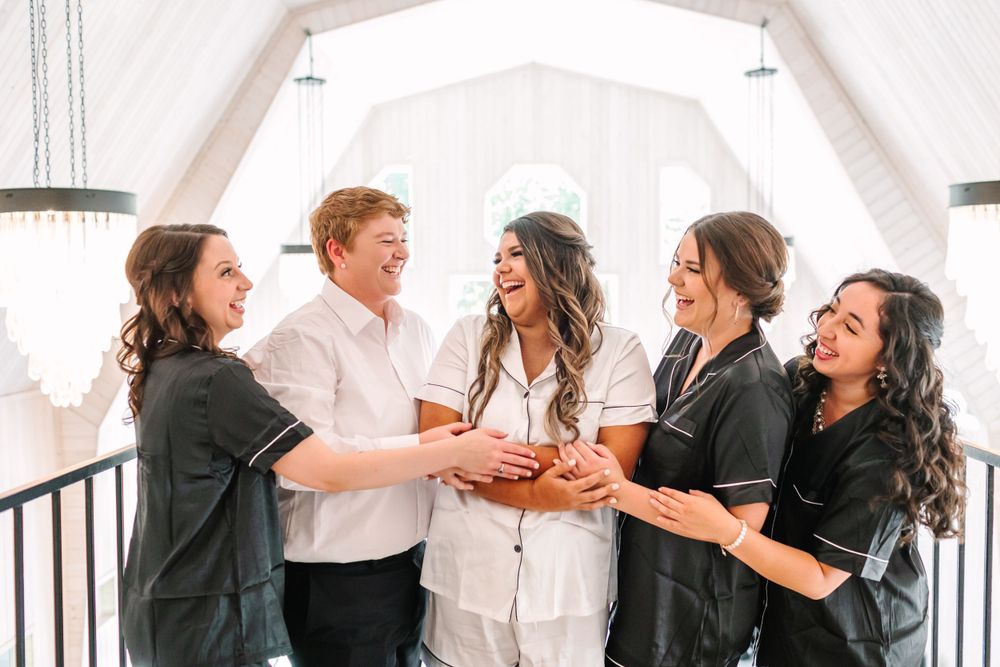 Group of wedding party members sharing a joyful moment together in a bright white room.