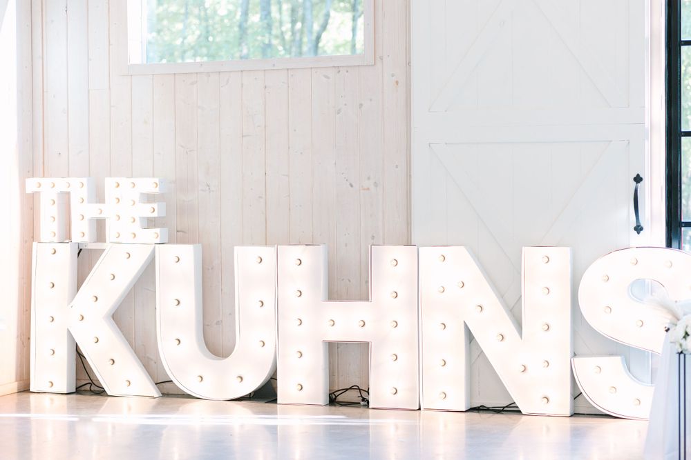 Large white marquee letters spell out 'THE KUHNS' against a light wood paneled wall.