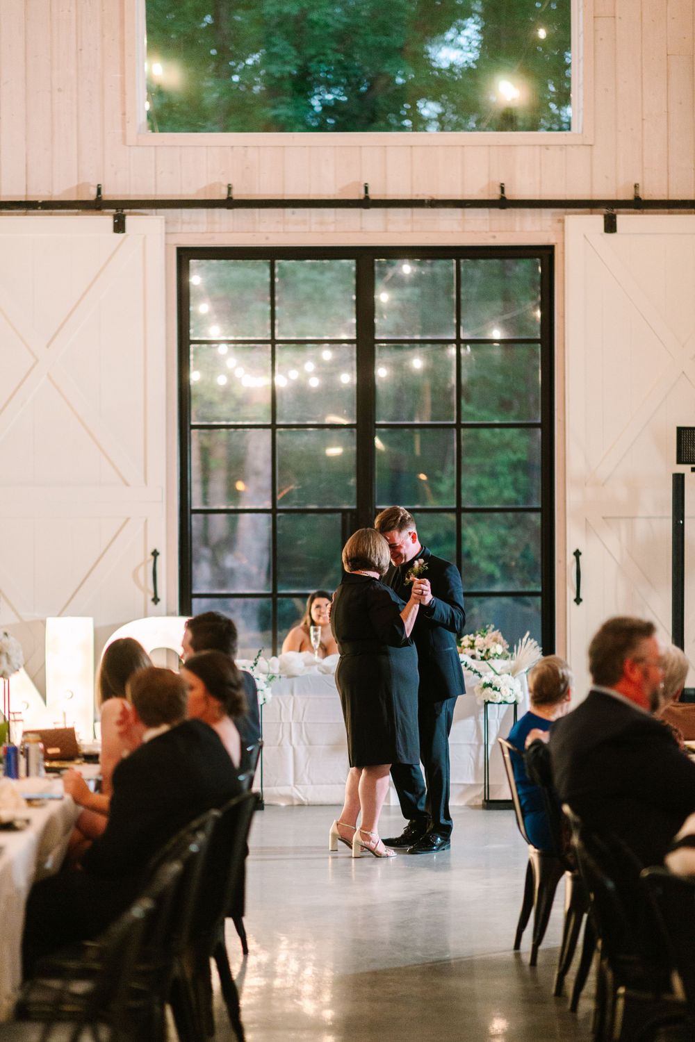 Elegant wedding reception dance in modern white venue with large windows and ambient lighting.