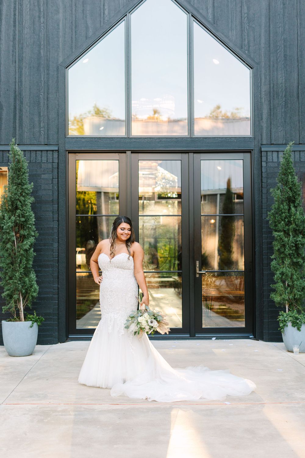 Bride in mermaid wedding dress poses in front of modern black building with geometric windows.