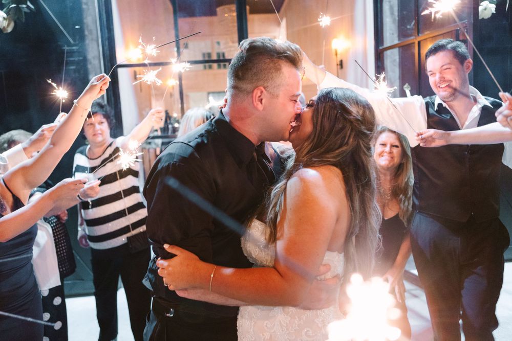 Wedding couple shares romantic first dance surrounded by celebrating guests with sparklers in an indoor venue.