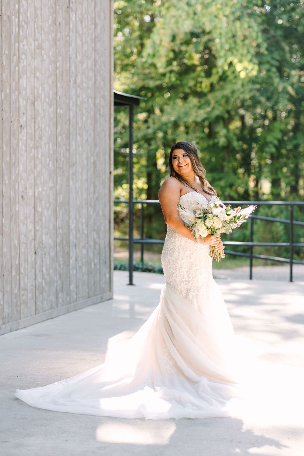Bride in fitted lace gown poses with bouquet against modern architectural backdrop.