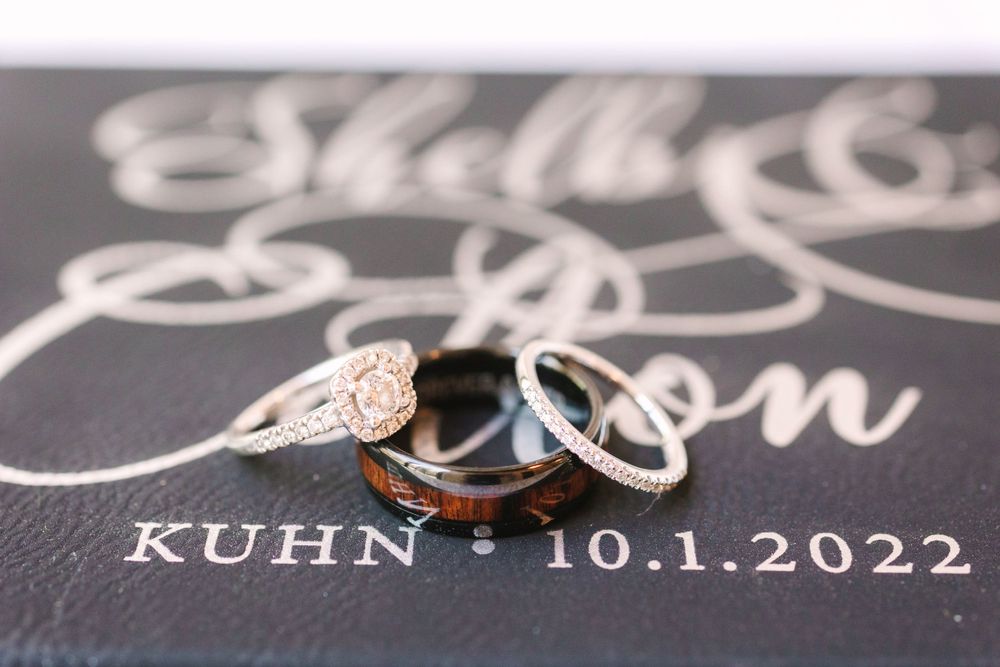 Wedding rings photographed on black paper with white calligraphy date inscription.