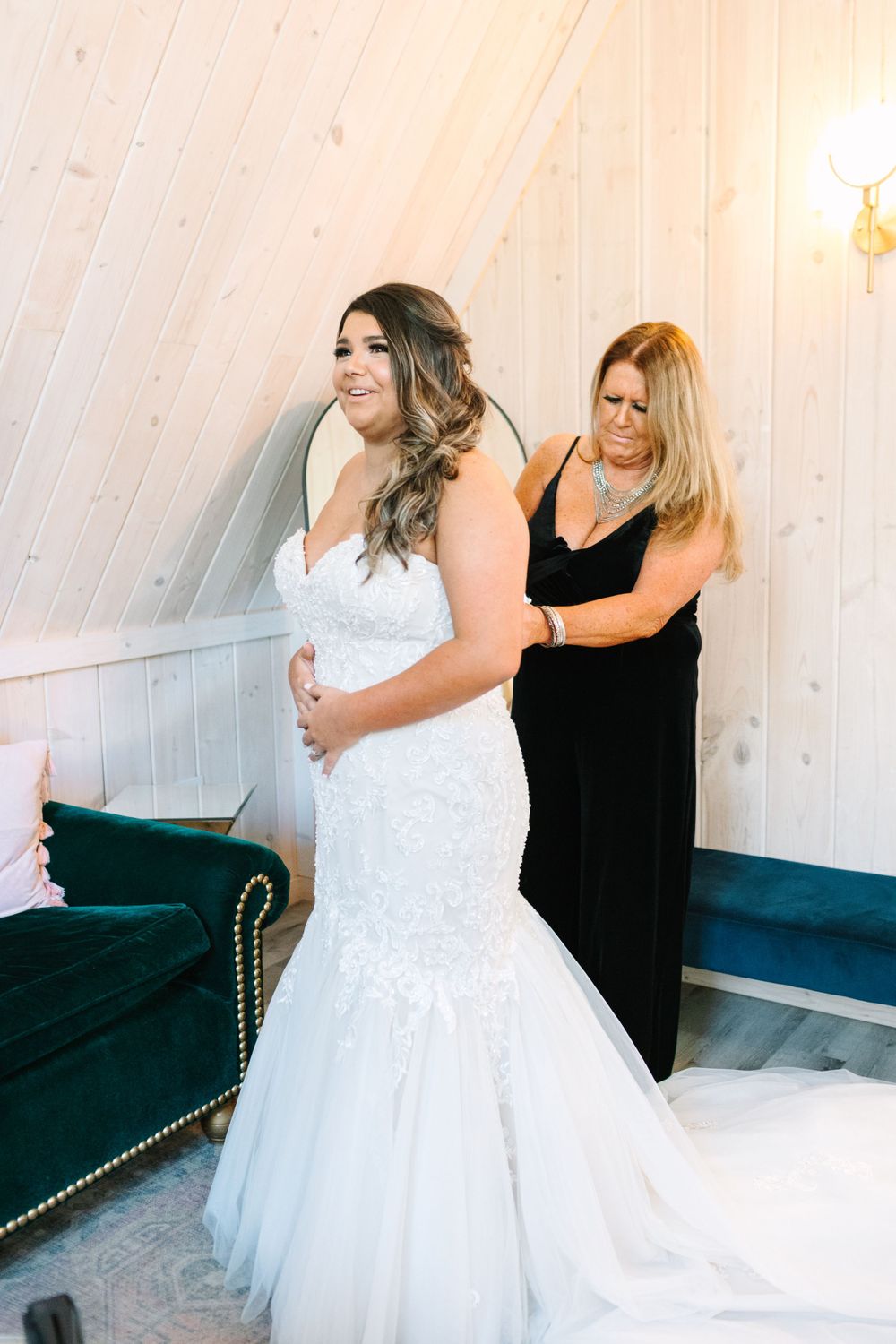 Bride in a mermaid wedding gown being helped with final dress adjustments.