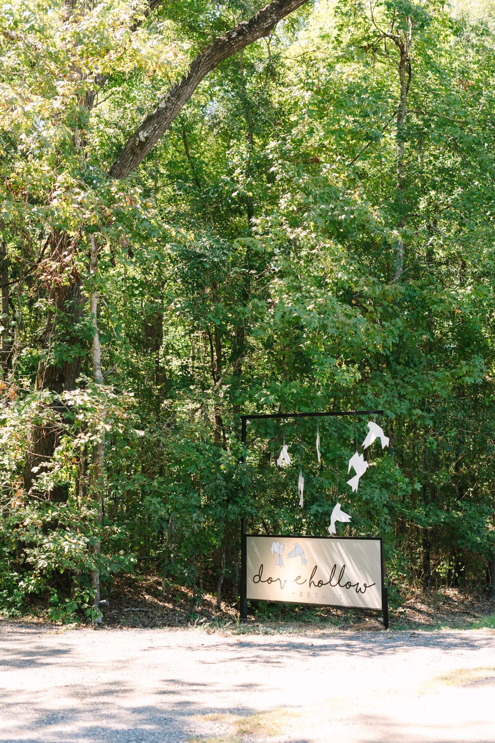 Rustic wedding venue sign surrounded by lush green trees and woodland setting.