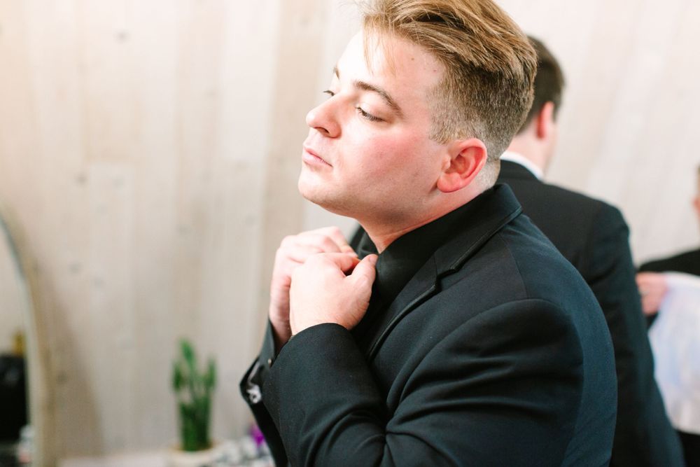 Groom adjusting his tie while getting ready in a black suit.