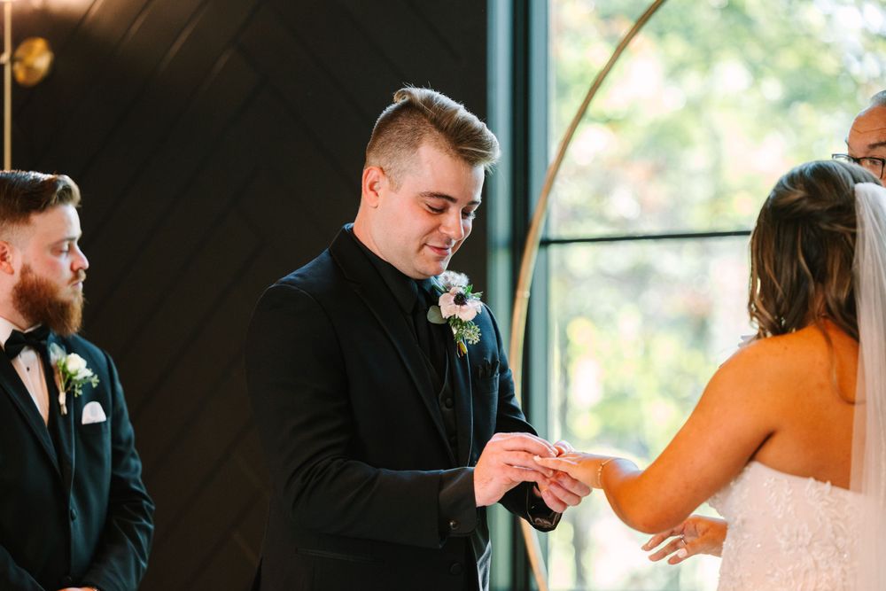 Exchange of rings during wedding ceremony with large window backdrop.