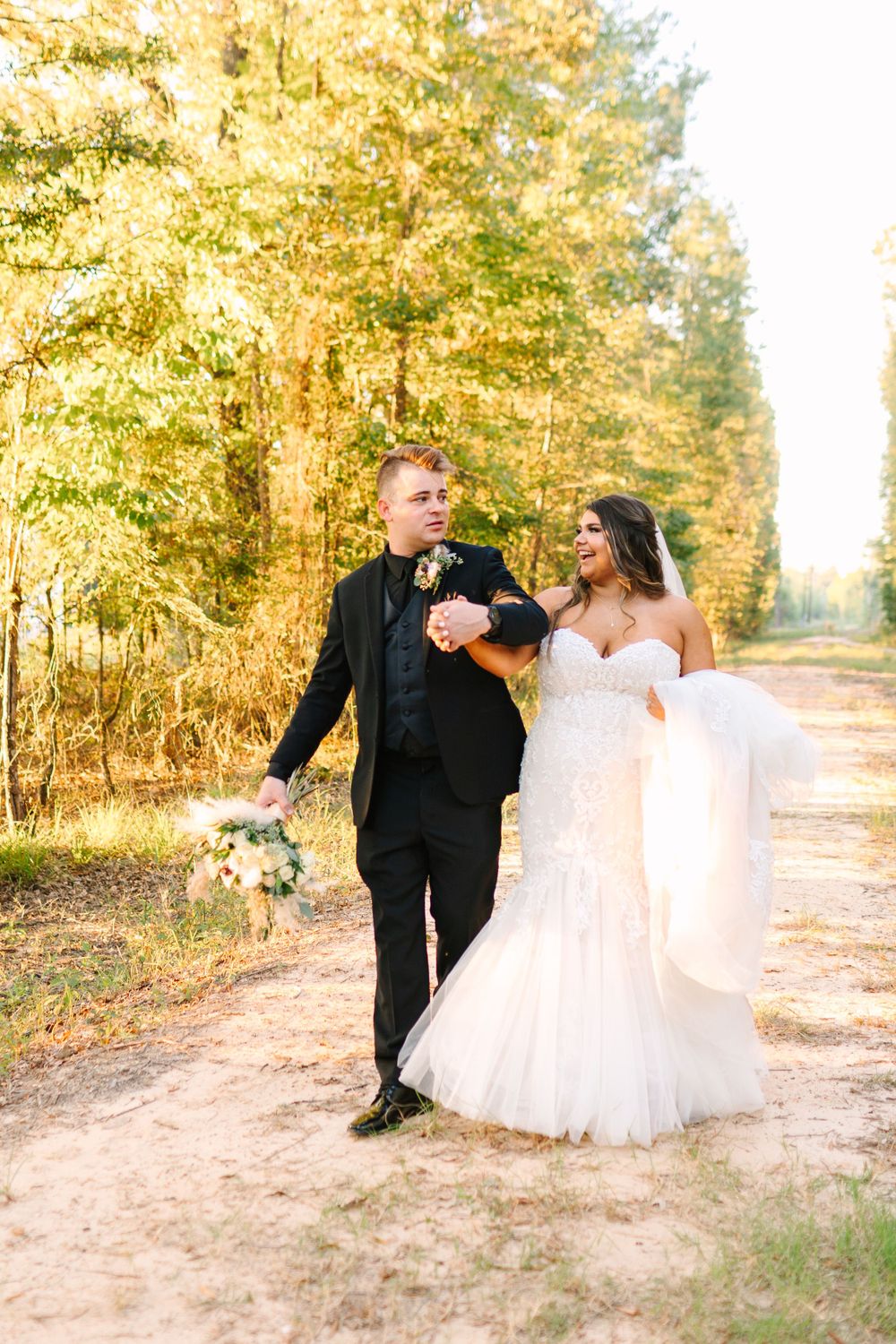 A couple walking together on a sunlit forest path during their wedding day.