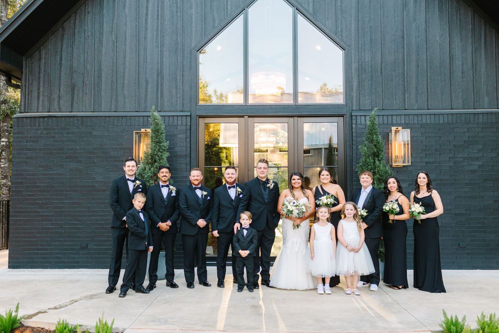 Wedding party lined up in front of modern dark barn venue with large glass windows.