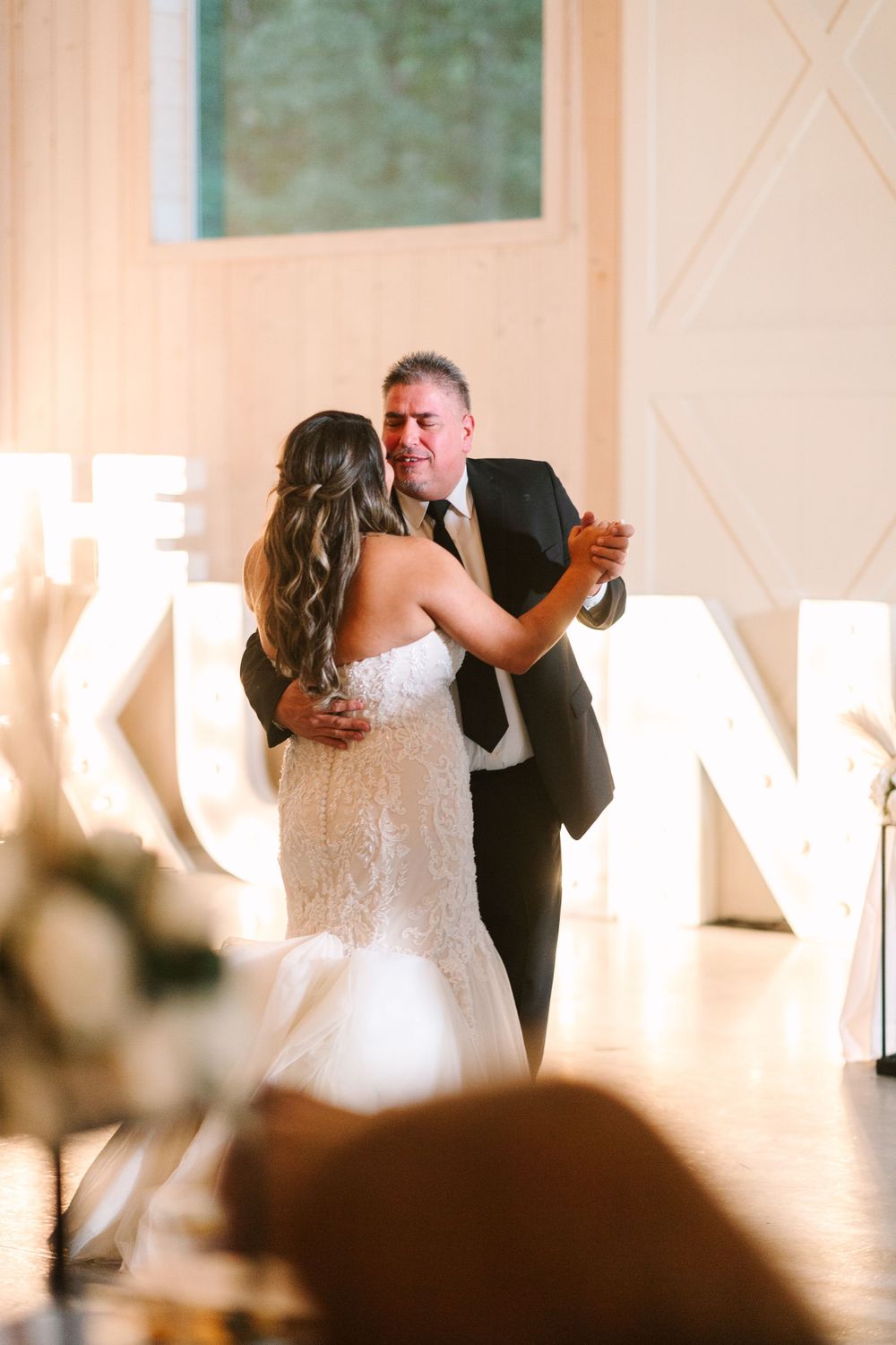 Couple sharing an intimate dance moment in front of decorative light-up letters at reception venue.