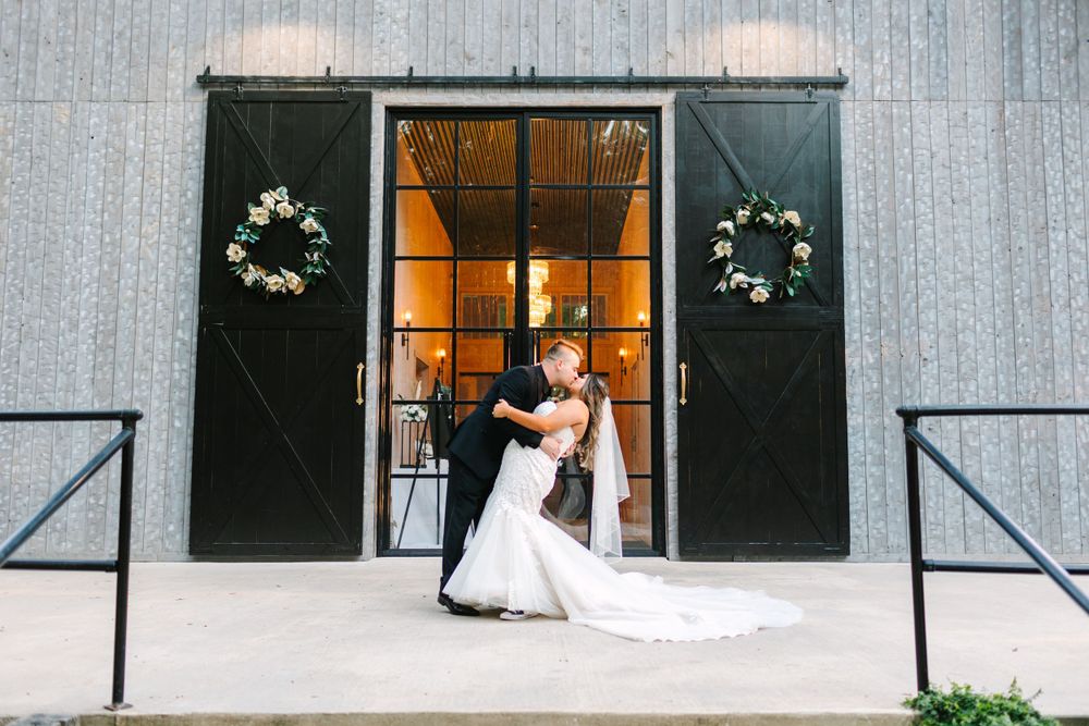 A wedding venue entrance with black barn doors decorated with white floral wreaths.