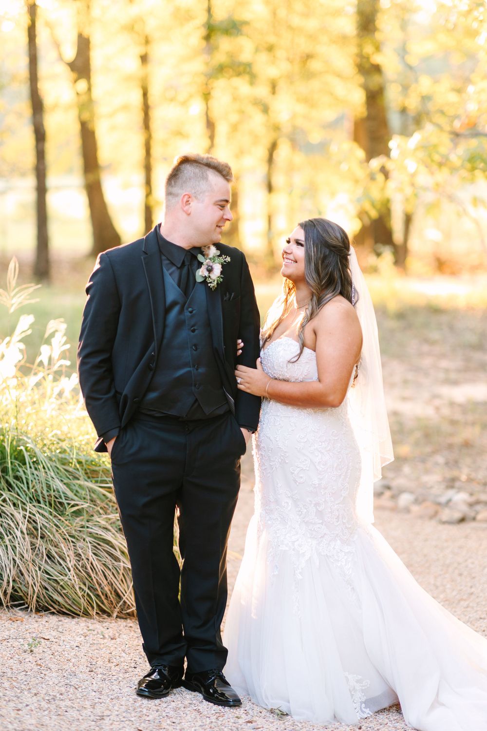 A romantic wedding photo of a couple sharing a joyful moment on a fall day with golden trees in the background.
