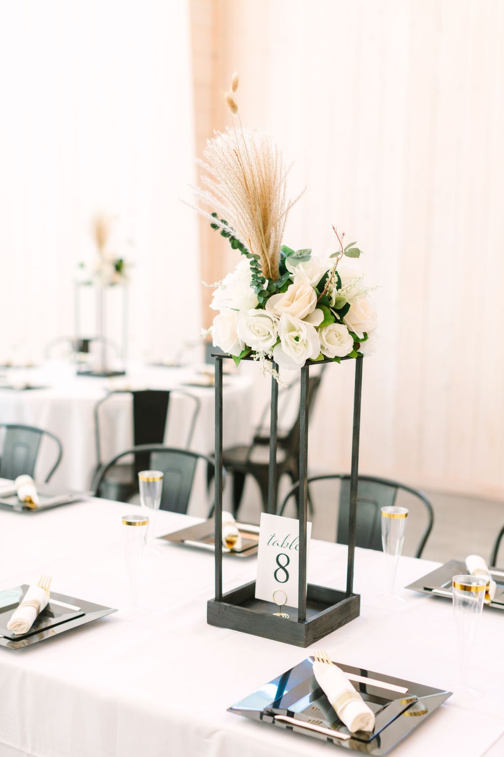 Modern wedding table centerpiece with white flowers and pampas grass in black stand.