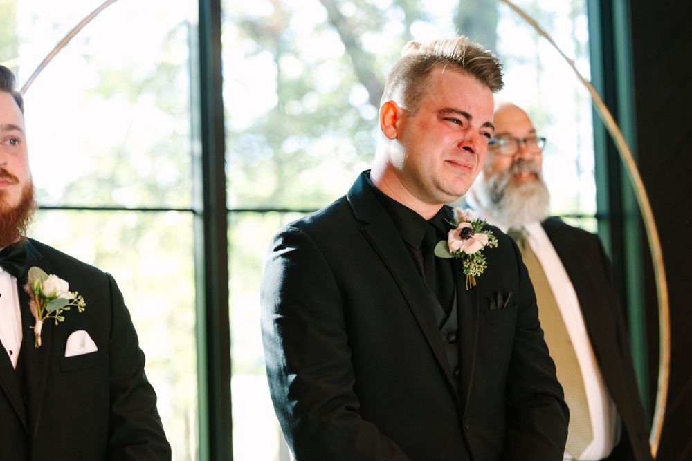 Emotional moment captured during wedding ceremony in front of large arched windows.