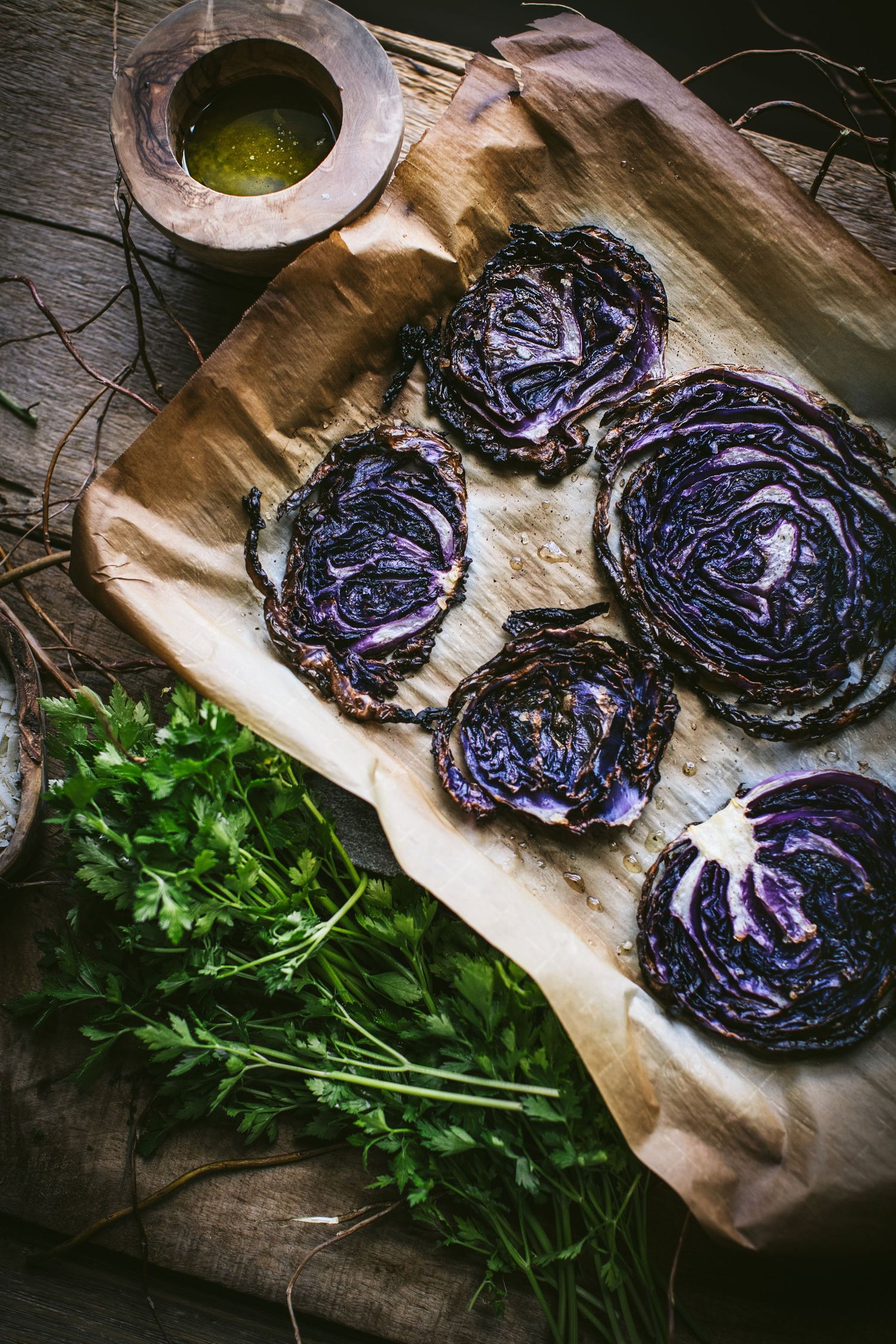 Roasted purple cabbage steaks on parchment paper with fresh parsley and herb dipping sauce.