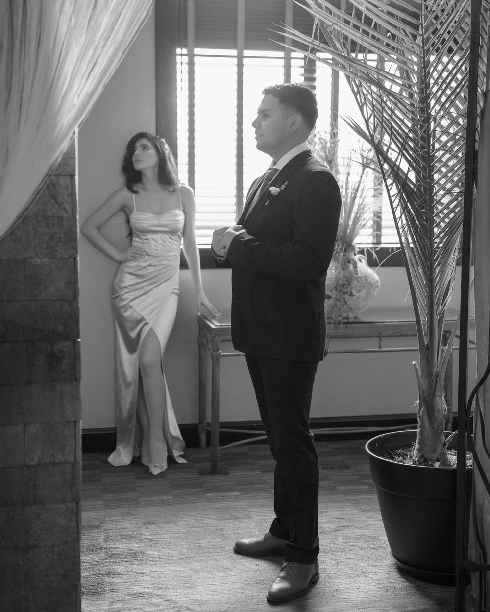 Couple in formal attire dances in an elegant indoor venue with palm trees in the background.