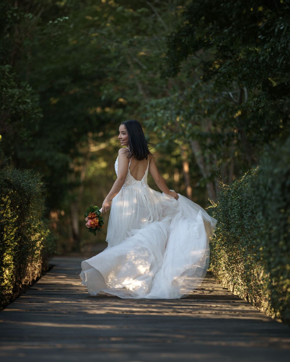 Bride in flowing white dress walks along garden path during outdoor photo session.