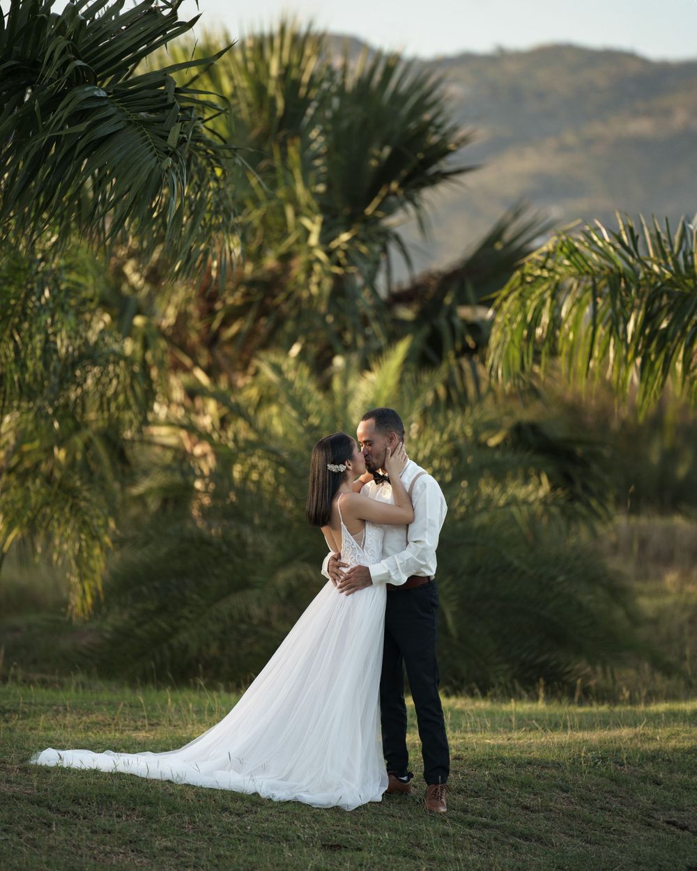 Wedding couple shares intimate moments against a backdrop of palm trees and mountains at sunset.