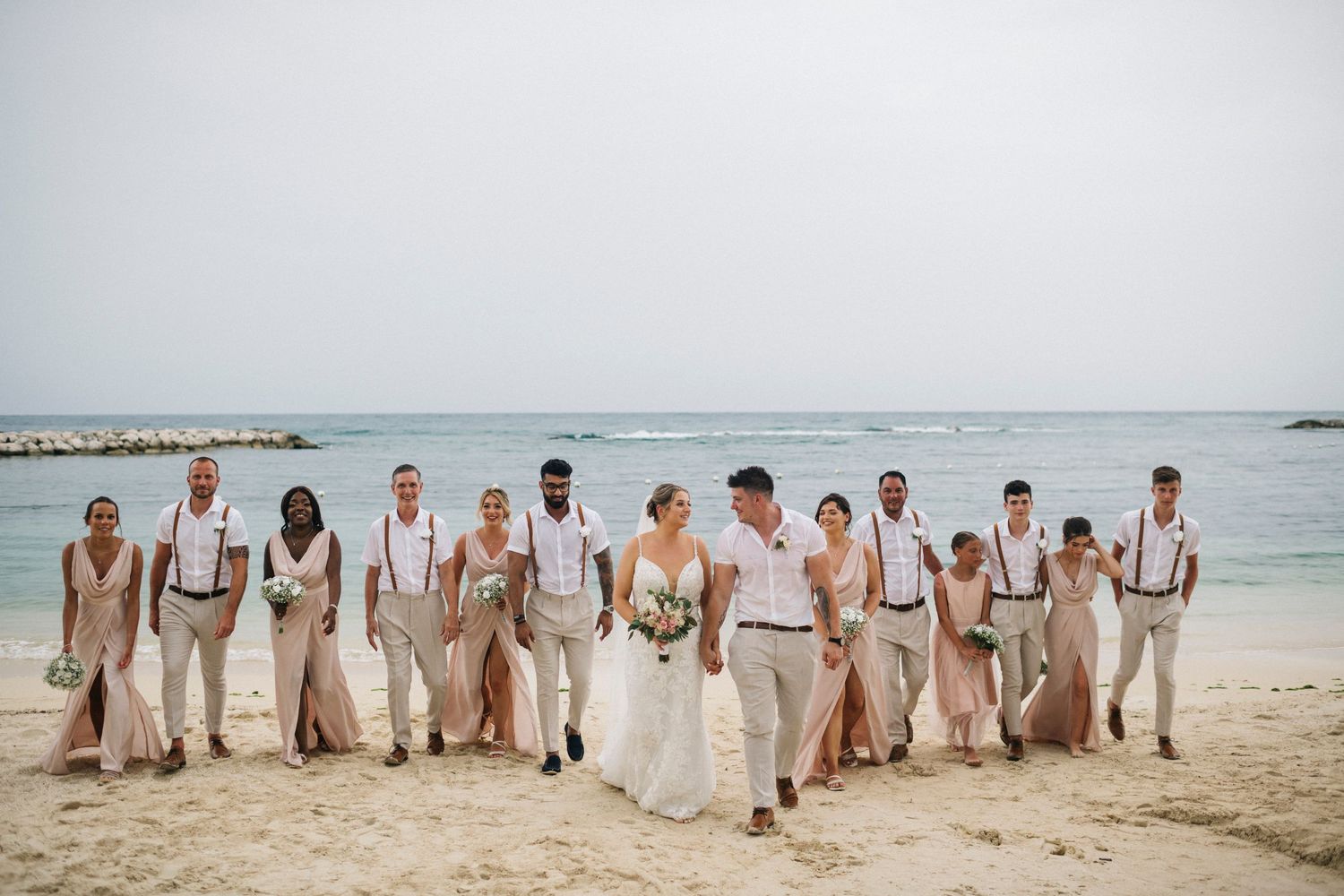 Wedding party lined up on beach wearing all white and beige attire.