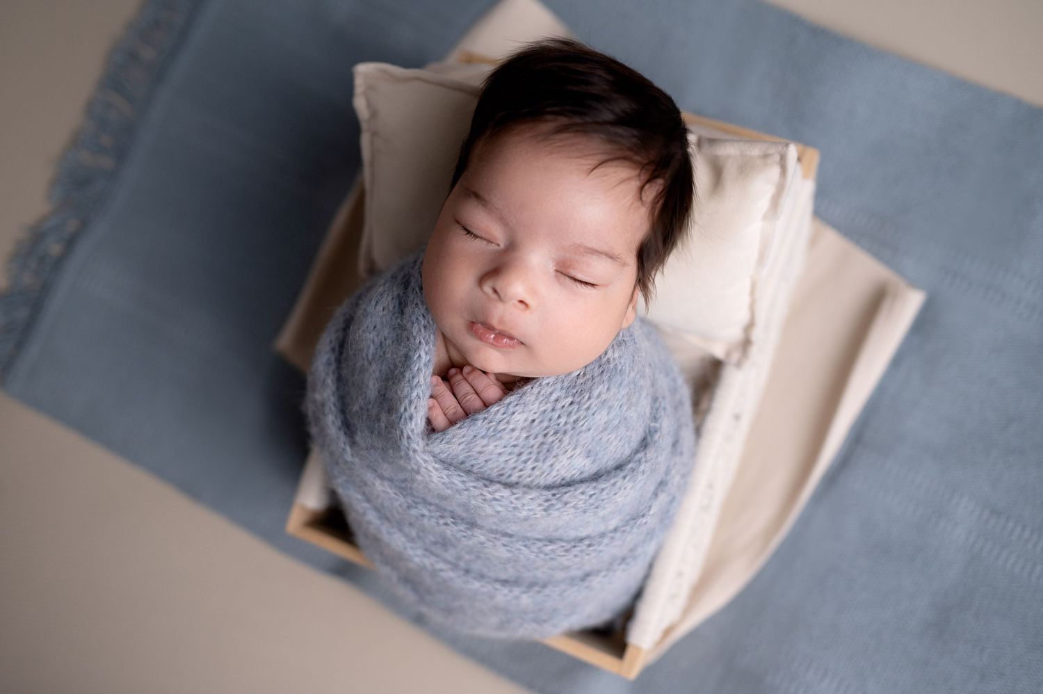 Sleeping newborn wrapped in soft gray knit blanket in wooden crate.