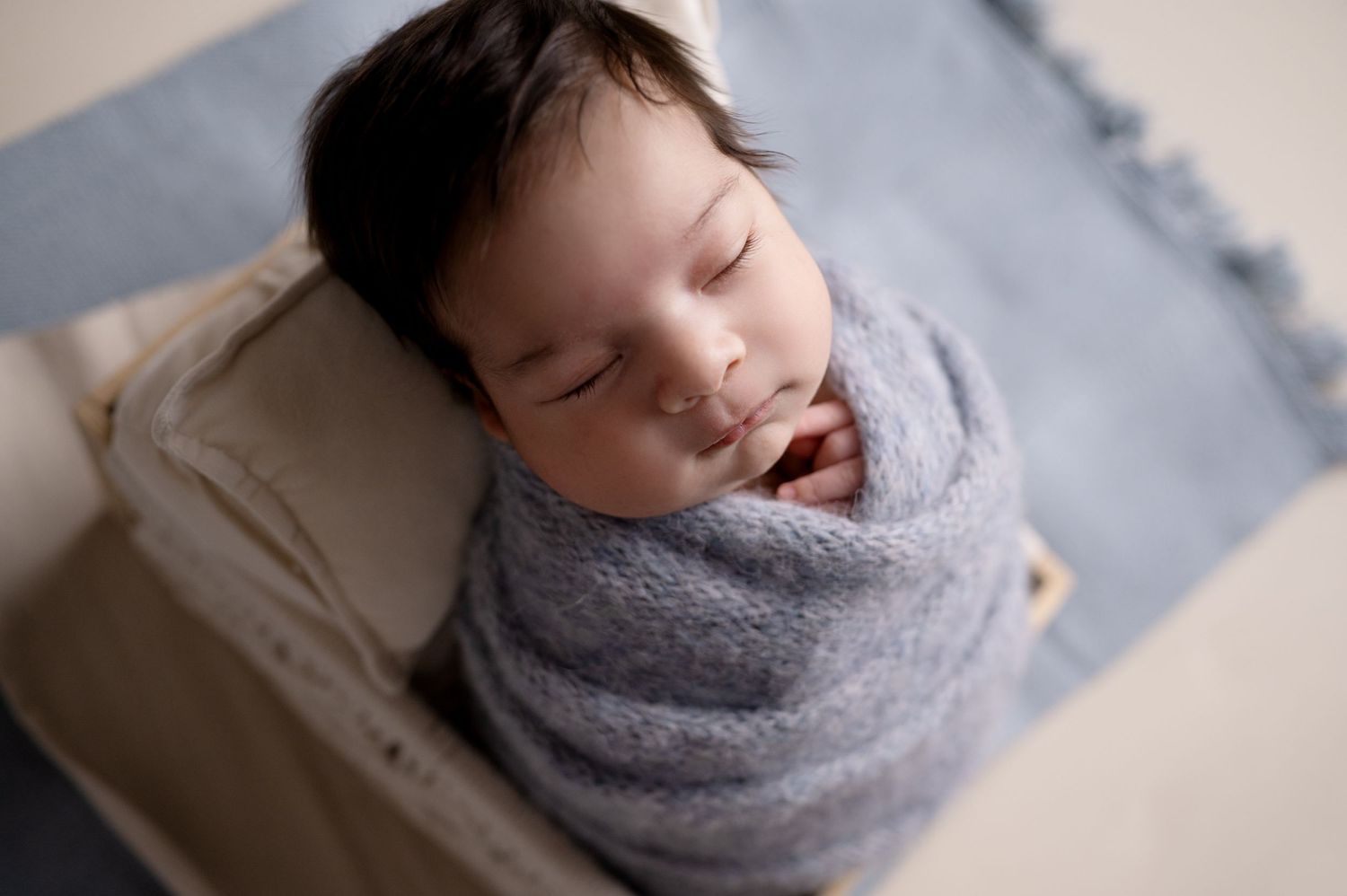 Overhead view of sleeping newborn wrapped in gray knit blanket on blue surface.