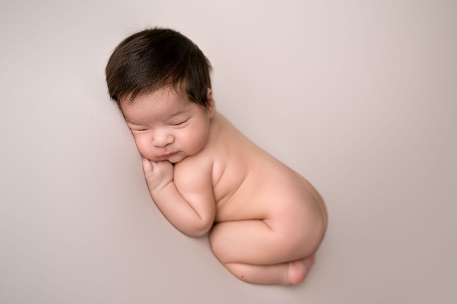 Peaceful sleeping newborn posed on neutral background.