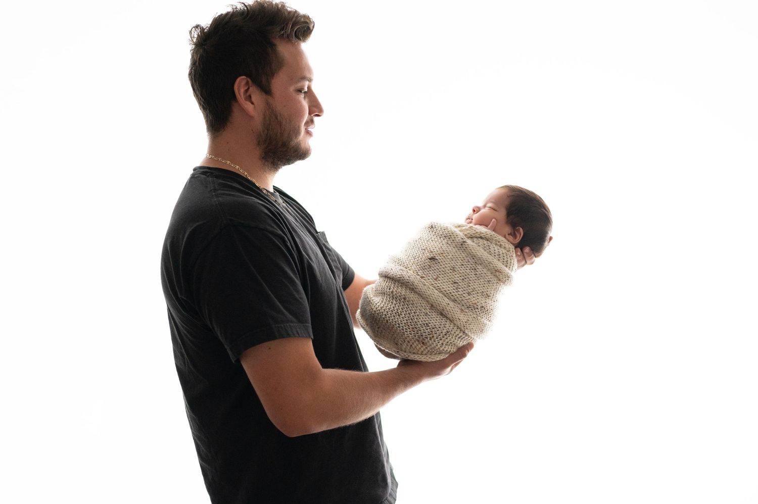 Parent in black shirt holding swaddled sleeping baby against white background.