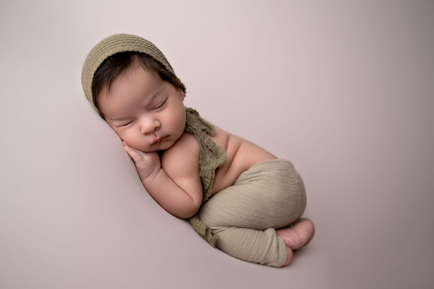 Peaceful newborn baby sleeping in neutral colored wrap and cap during professional photo session.