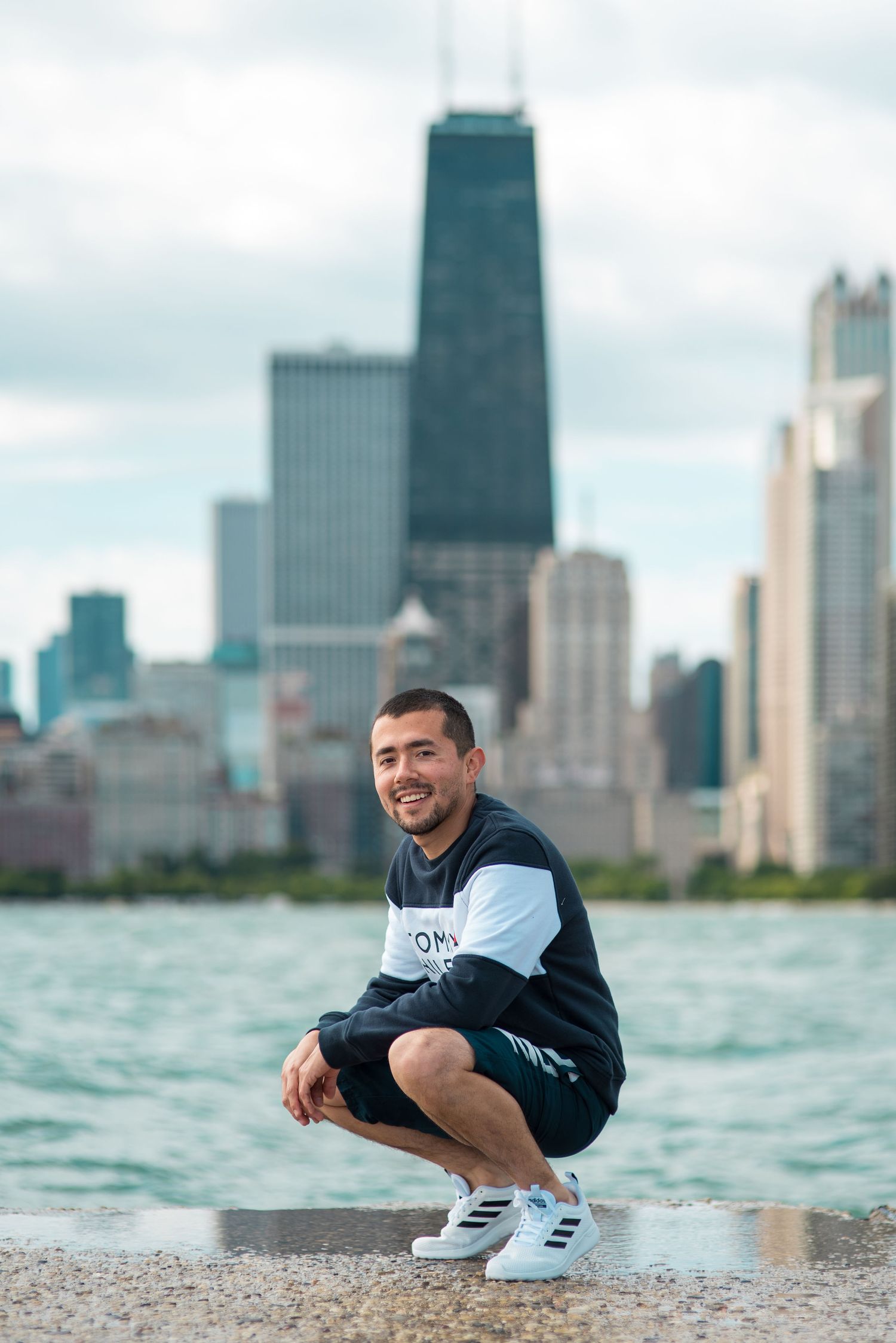 Person crouching by Chicago waterfront with John Hancock building and skyline in background.
