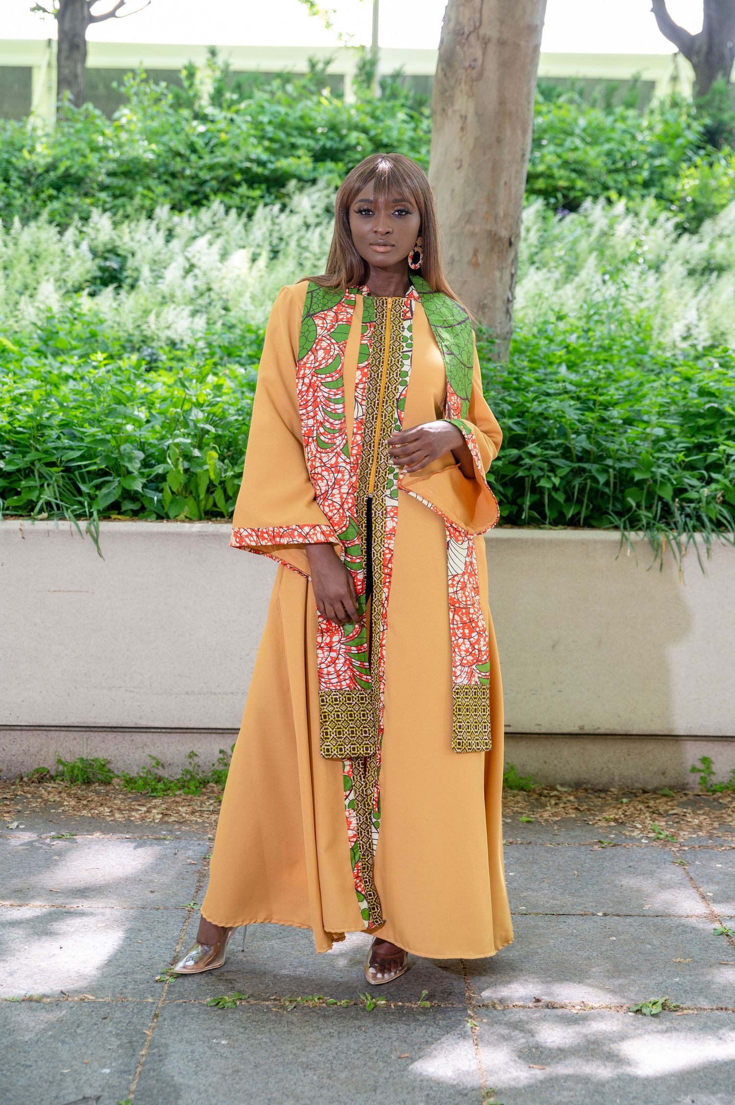 Fashion photo of orange flowing dress with floral accents against green garden backdrop.