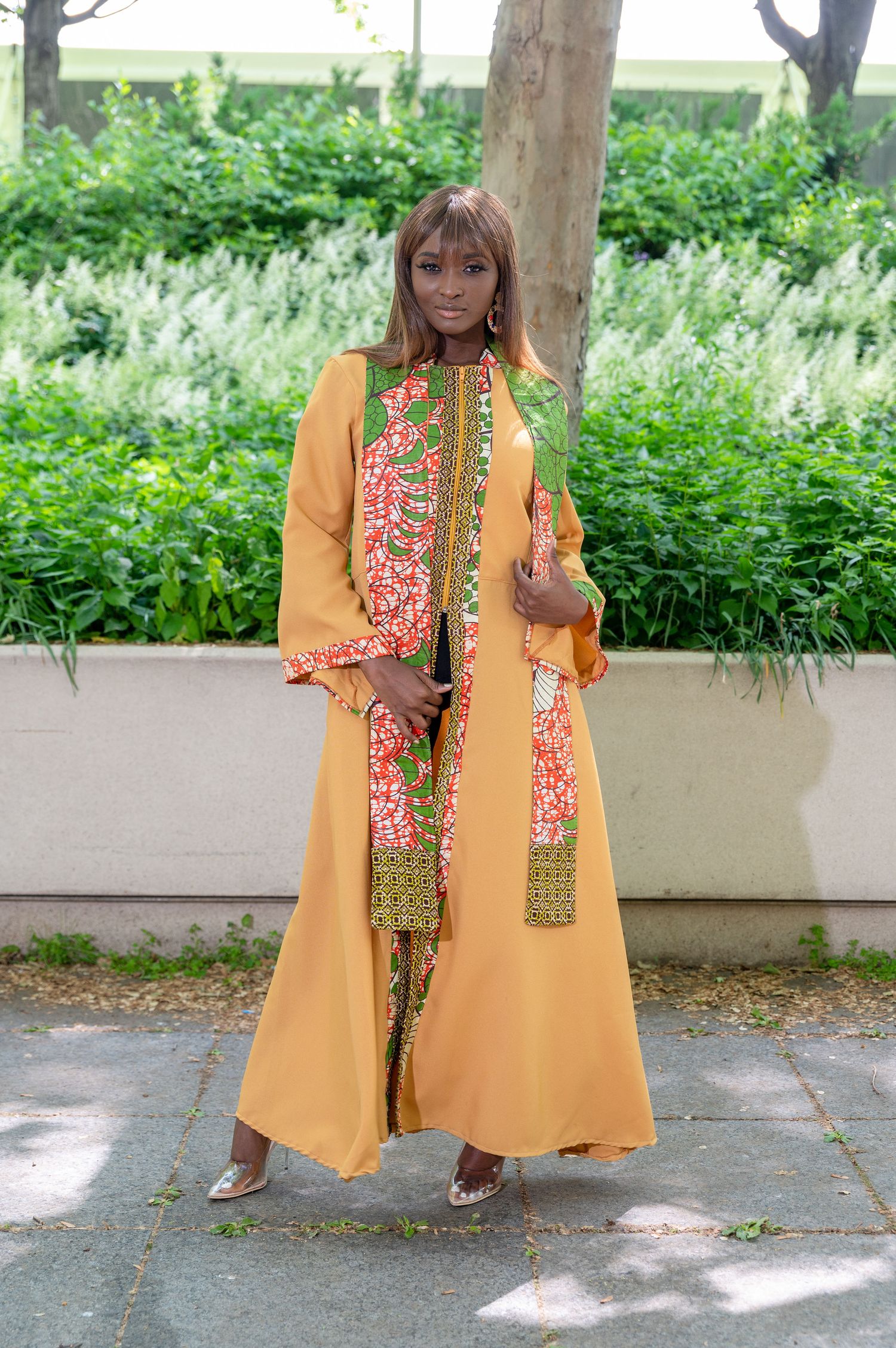 Model showcasing orange traditional dress with floral details in garden setting.