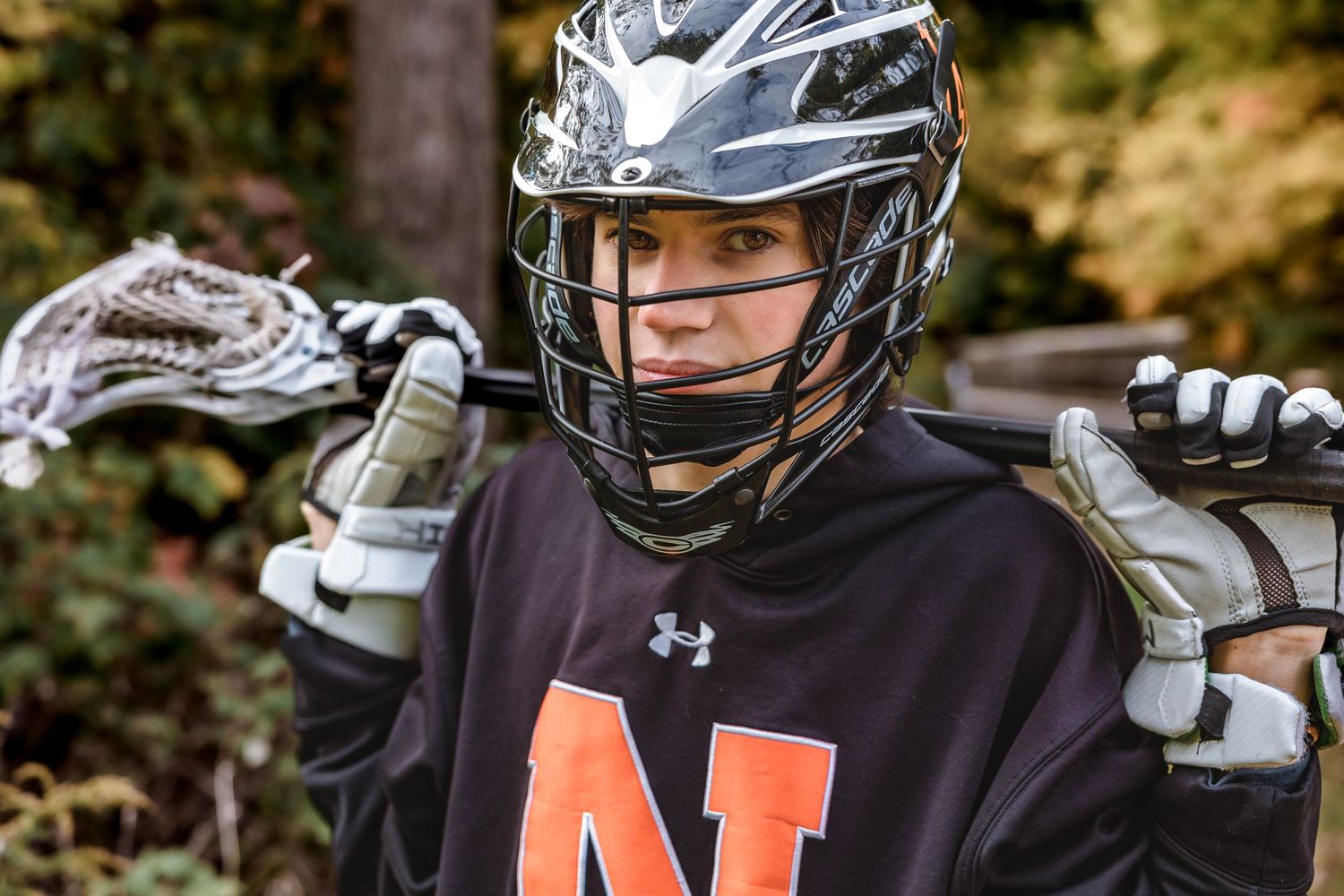 Lacrosse player in black Under Armour jersey holding equipment and wearing protective helmet and gear.