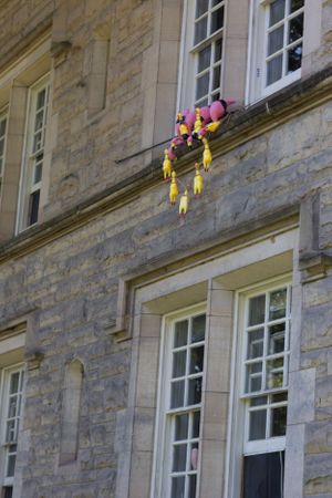 Colorful decorative balloons and streamers hanging from a stone building's window ledge.