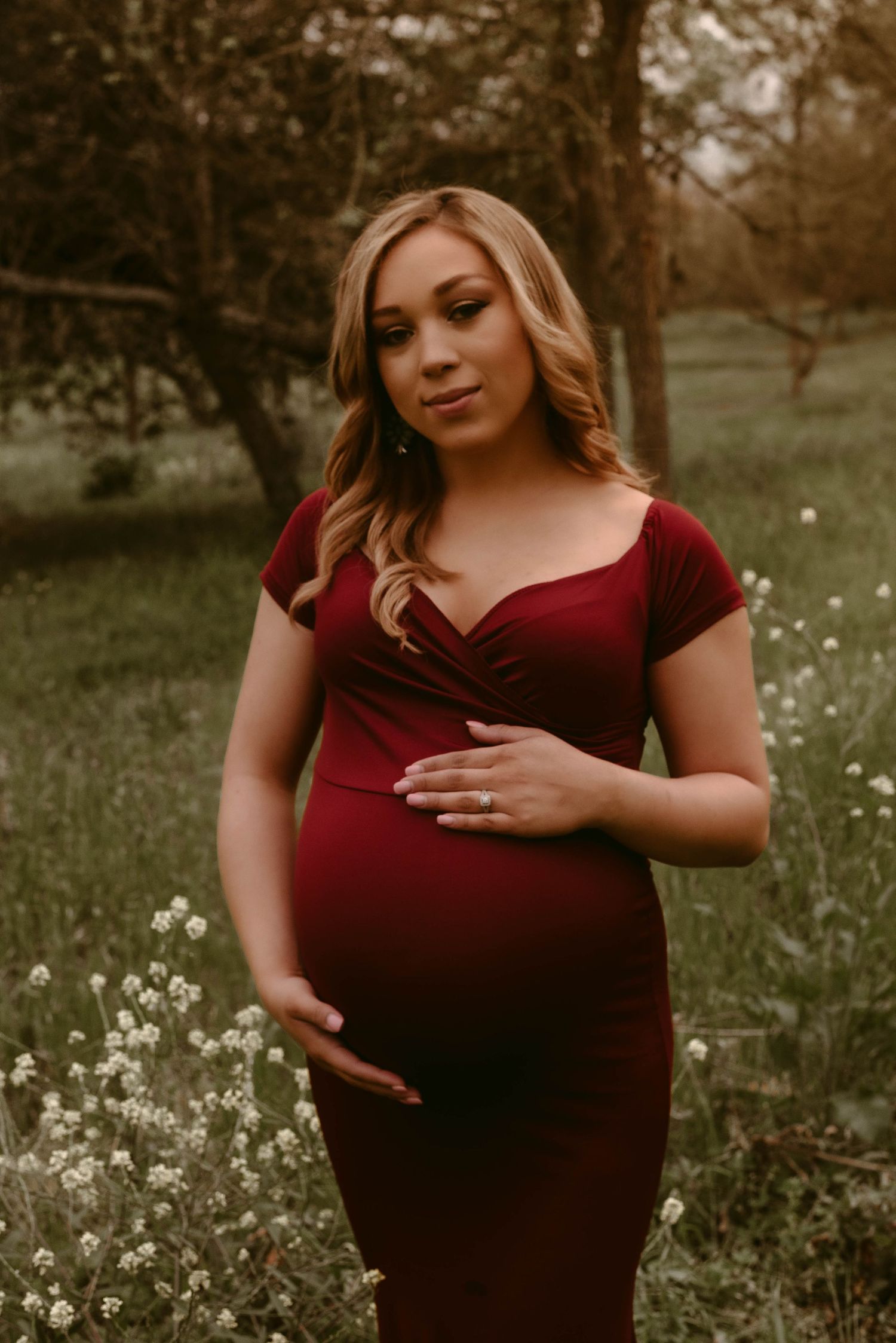 Expecting mother in red dress poses gracefully in field of spring flowers.