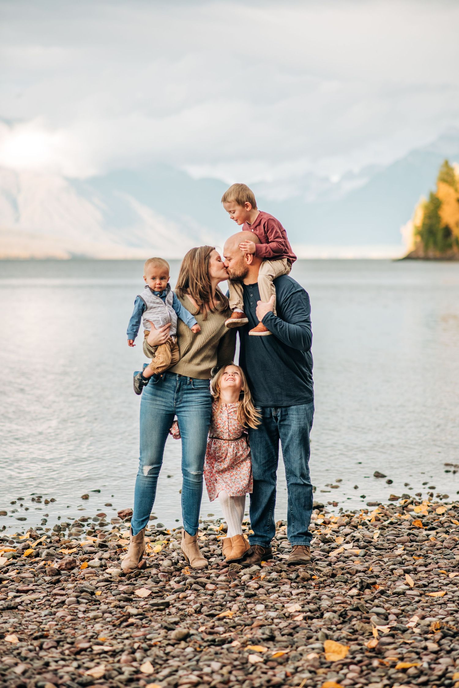 A family shares a tender moment together on a rocky beach with mountains in the background.