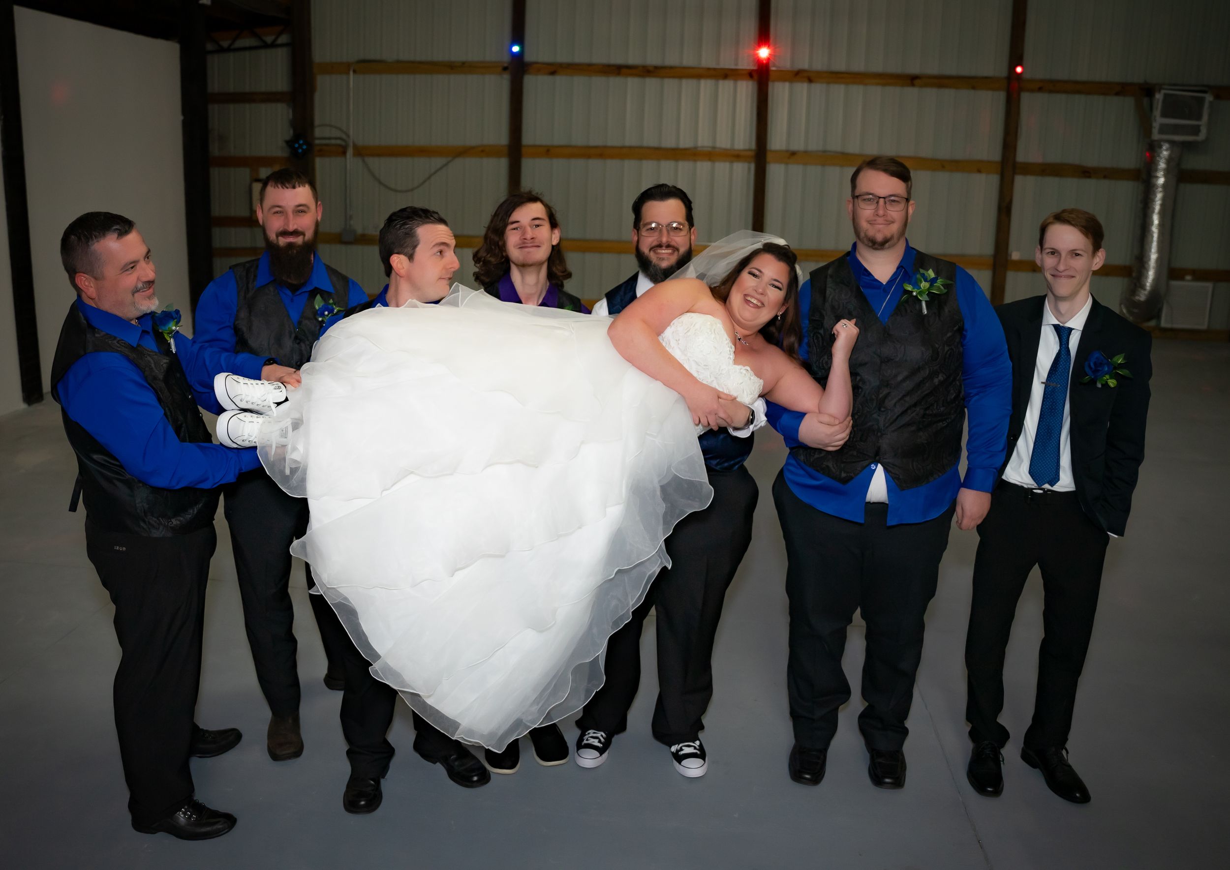 Wedding party poses playfully while lifting the bride in a group photo.