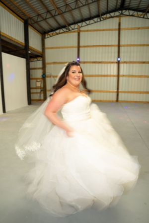 A bride twirls in a flowing white ballgown in an indoor venue.
