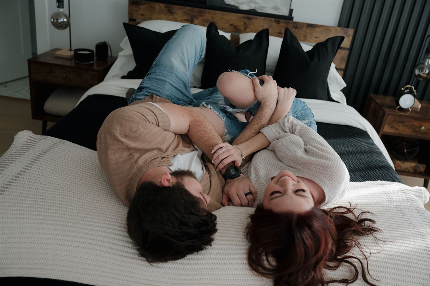 Couple lying on a modern bed with black and white decor sharing an intimate moment.