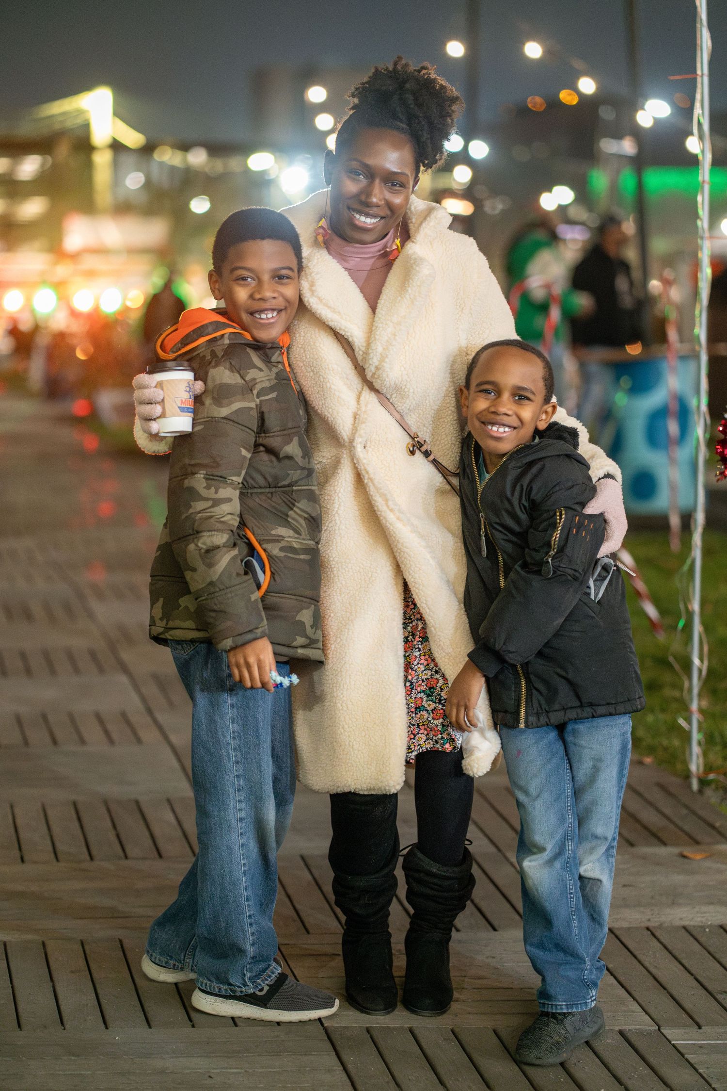 A family enjoying an evening outing along a boardwalk with city lights in the background.