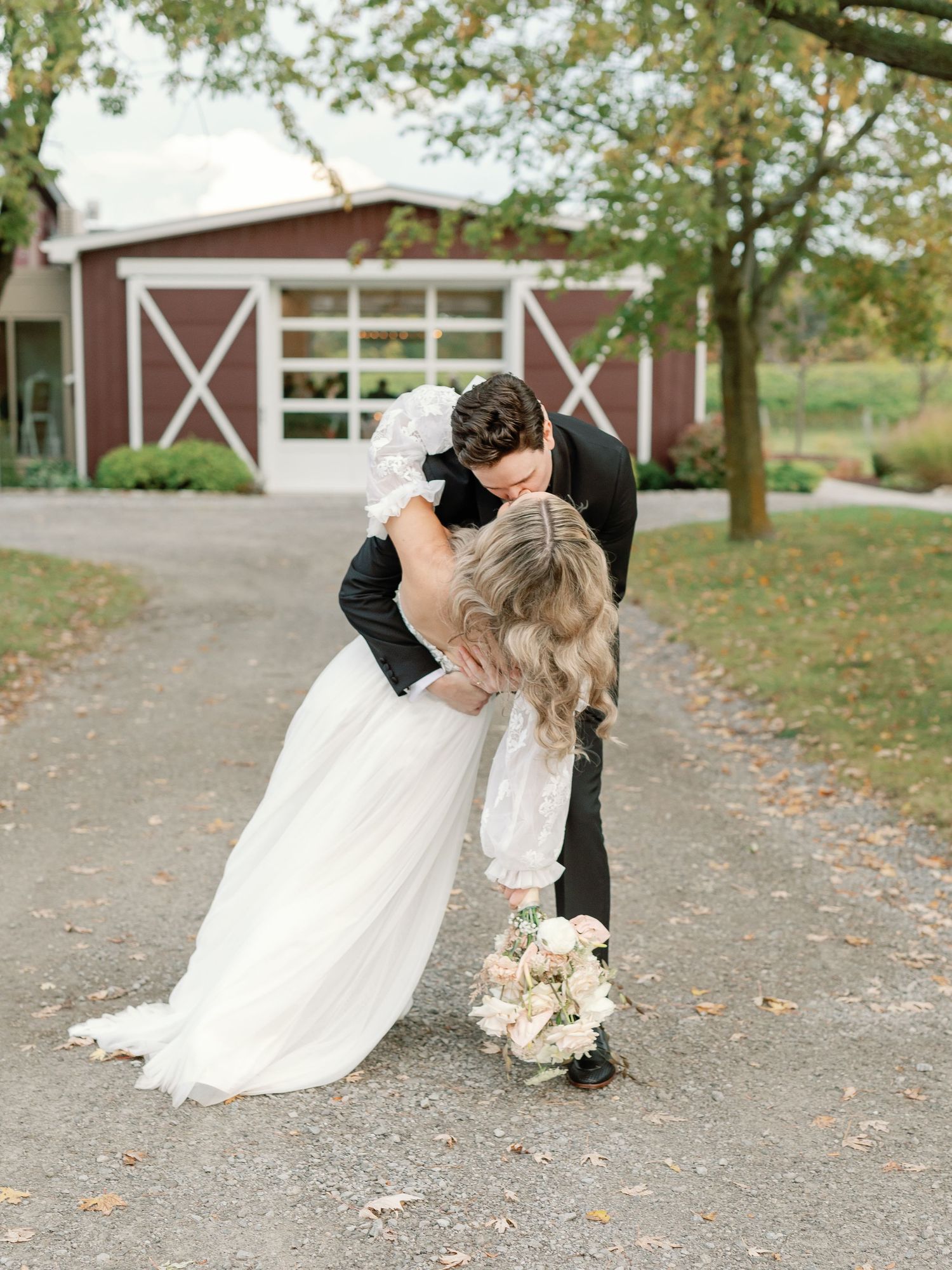 The bride has an arm hanging with her bouquet and the other around the grooms neck as he dips her into a deep kiss.