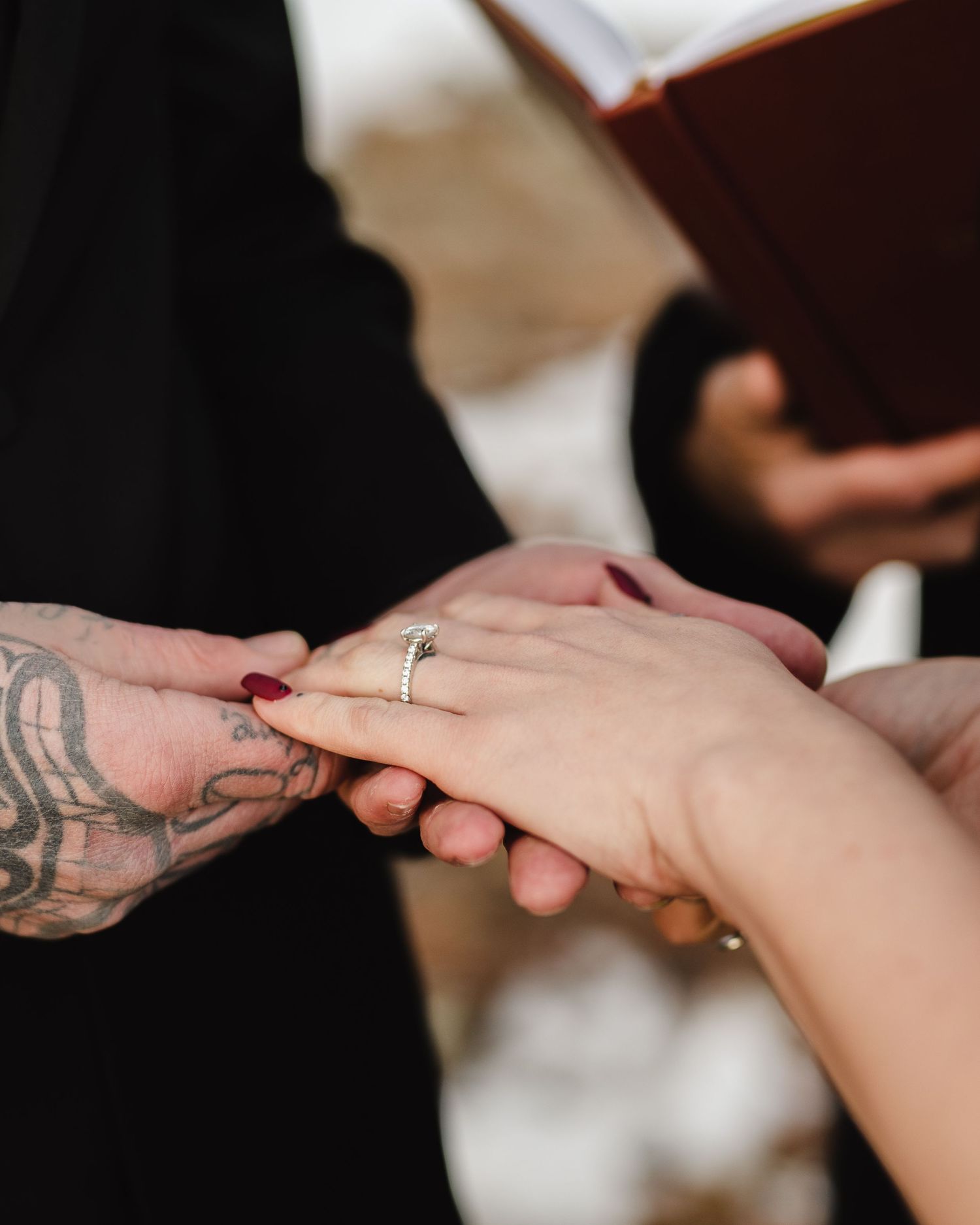 Close-up of hands exchanging wedding rings, with one hand showing a detailed tattoo.
