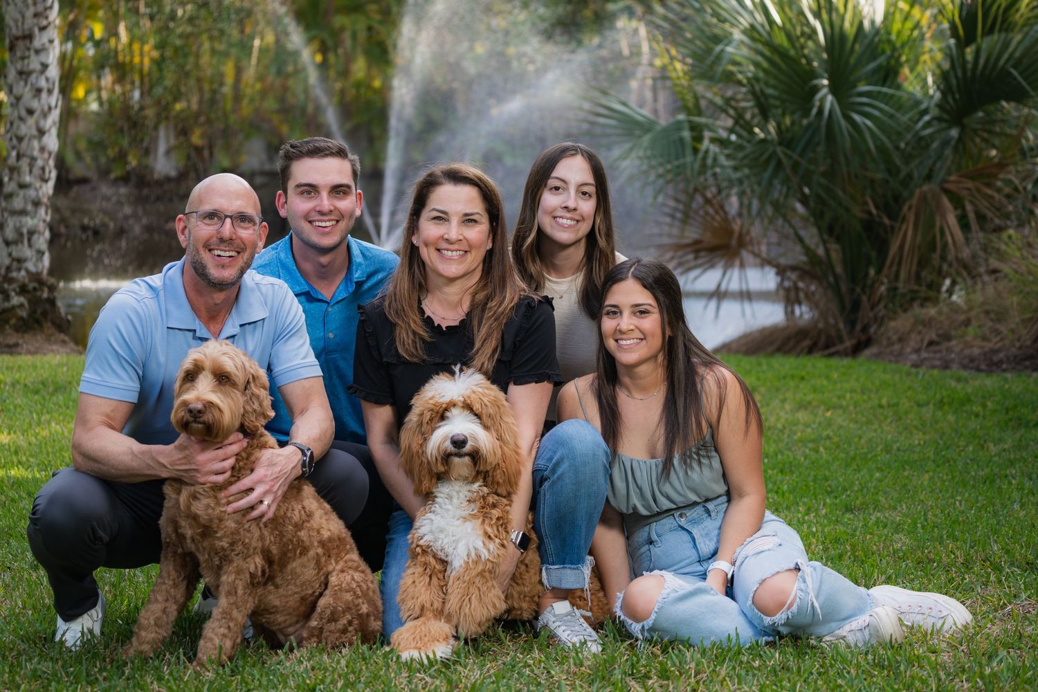 Family portrait with two dogs on a grassy lawn with palm trees and fountains.
