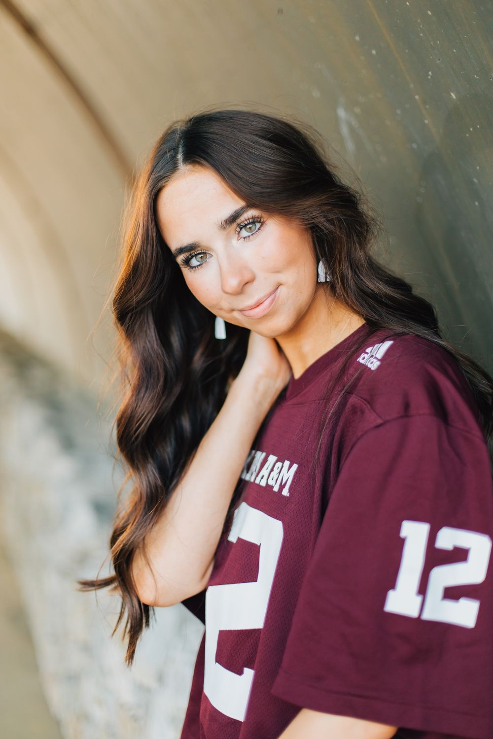 Portrait of woman in maroon sports jersey leaning against wall with long dark wavy hair.