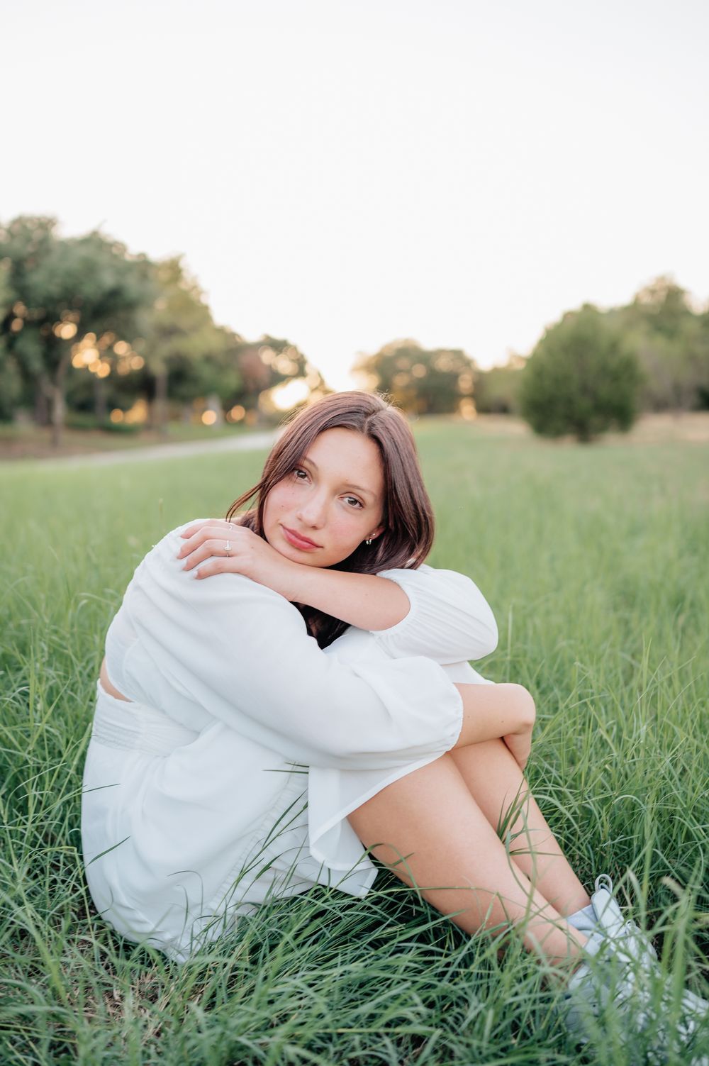 Person in white dress sits peacefully in tall grass during golden hour.