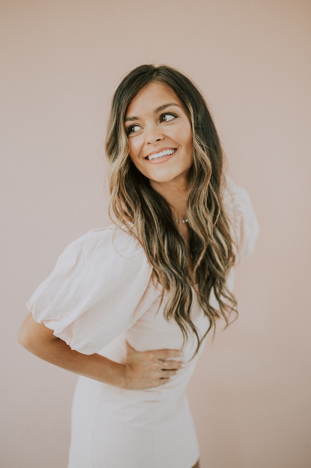 Side profile portrait of person in white dress with flowing hair against pink backdrop.