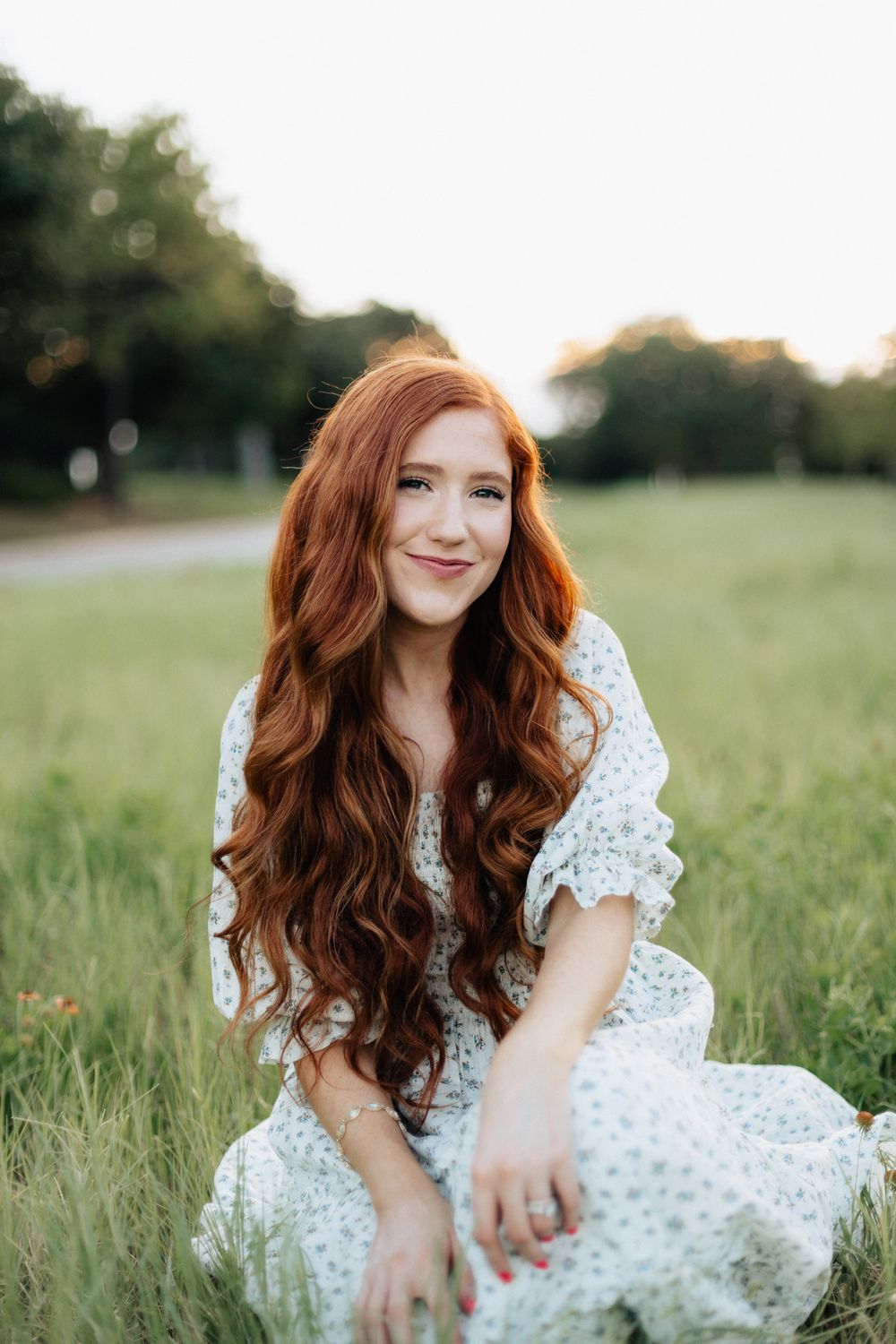 Person in white lace dress sitting in sunny field with long flowing hair.