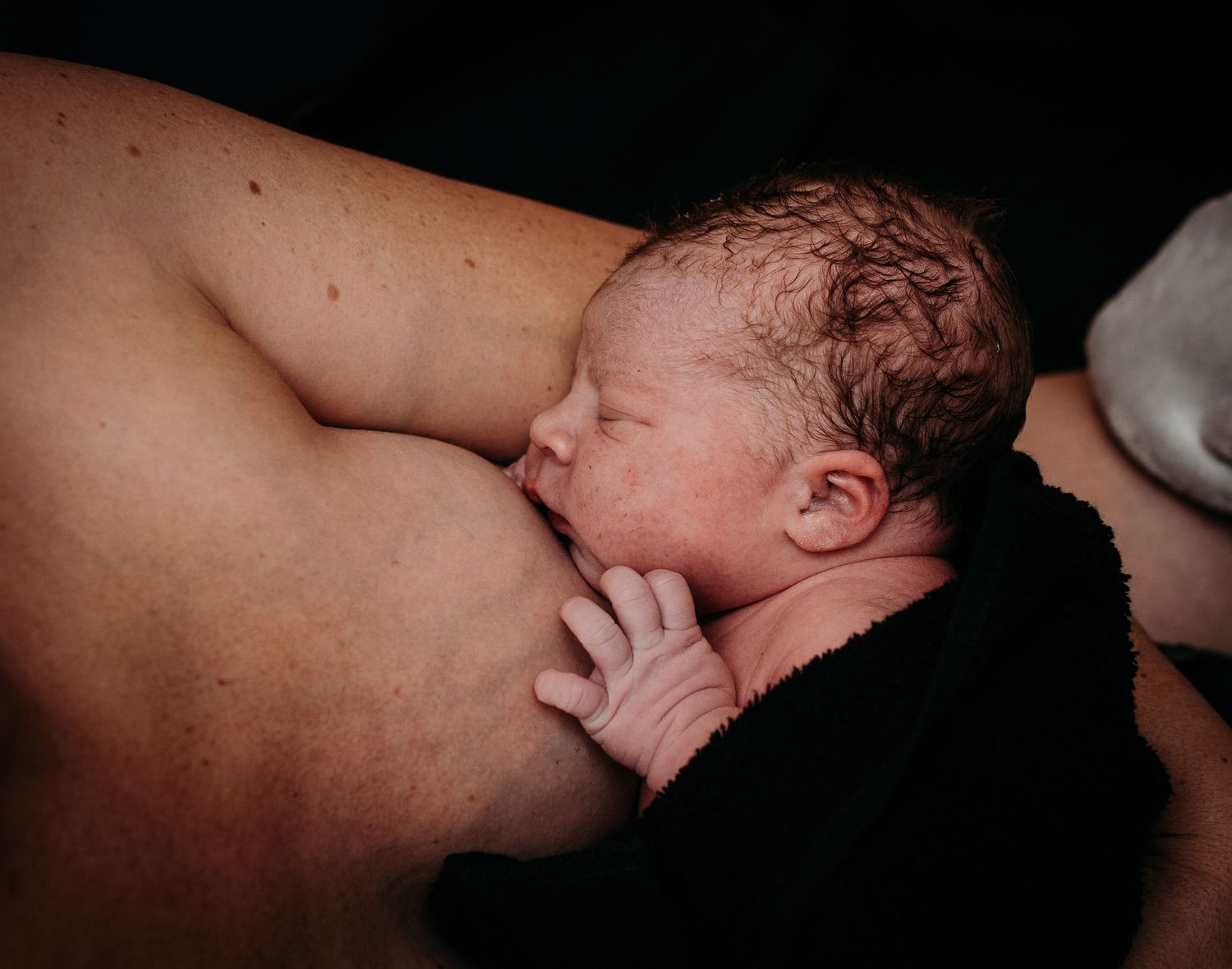Close-up view of a newborn baby's face against a dark background.